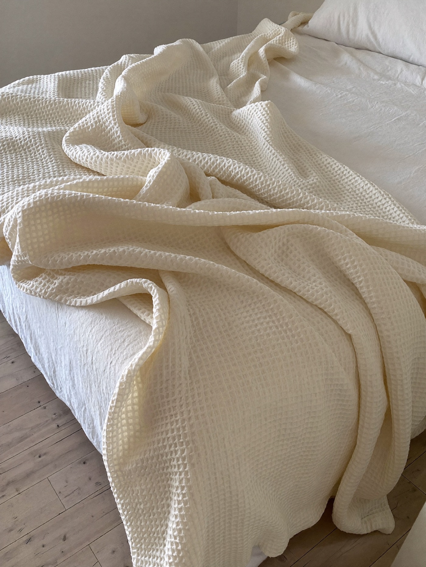 The muslin blanket in Shell, draped over the foot of a linen bed